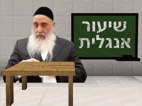 a man with a beard sits at a wooden table in front of a green board that says ' hebrew '
