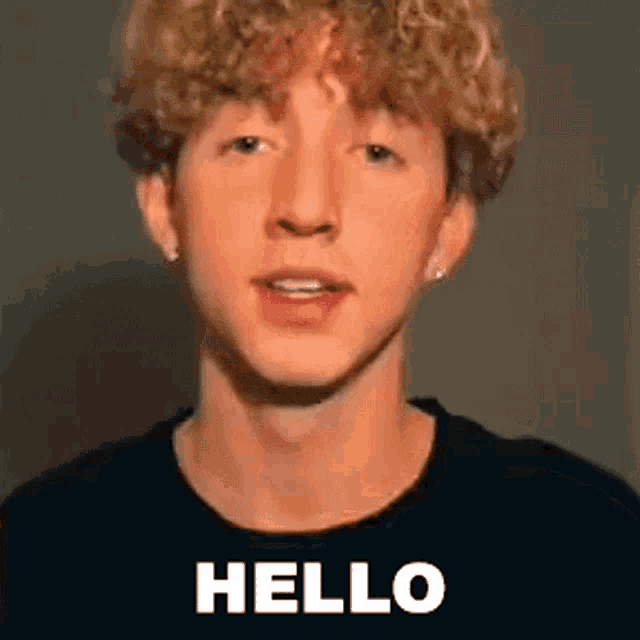 a young man with curly hair is wearing a black shirt and saying `` hello '' .
