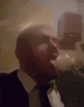 a man in a suit and tie is smoking a cigarette in a dark room .