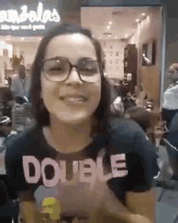 a woman wearing glasses and a shirt that says double is smiling .