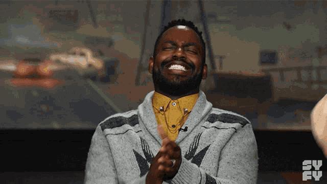 a man wearing a grey sweater and a yellow shirt is laughing and clapping