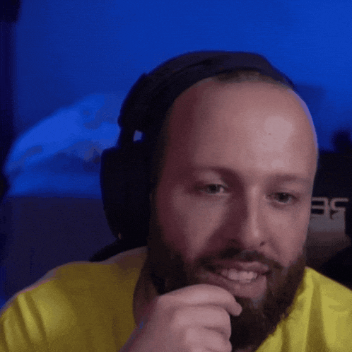 a bald man with a beard wears headphones and a yellow shirt
