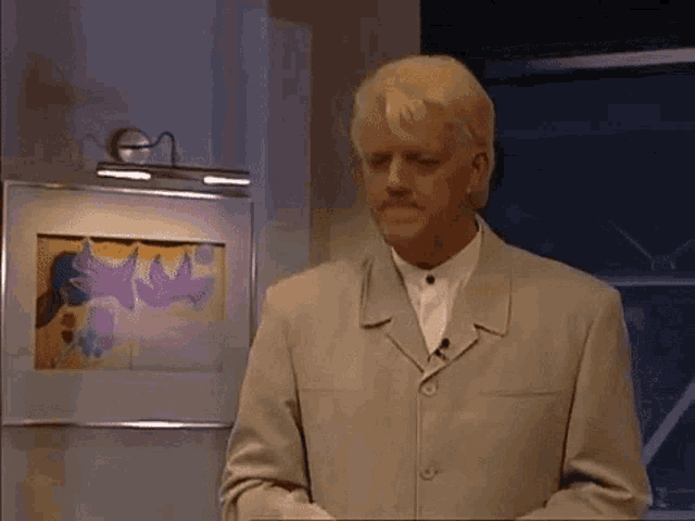 a man in a suit and white shirt is standing in front of a framed picture .