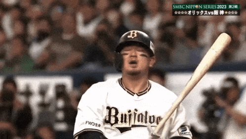 a baseball player wearing a buffalo jersey holds a bat in front of a crowd