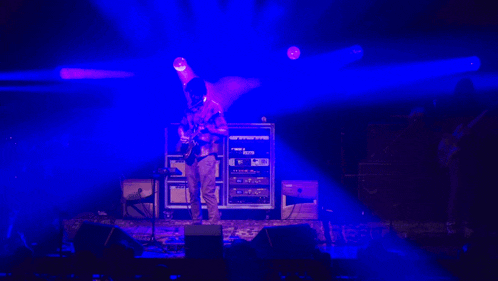 a man playing a guitar on a stage with a blue light behind him