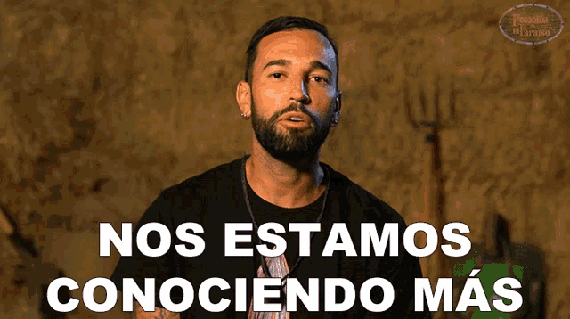 a man with a beard stands in front of a sign that says nos estamos conociendo mas