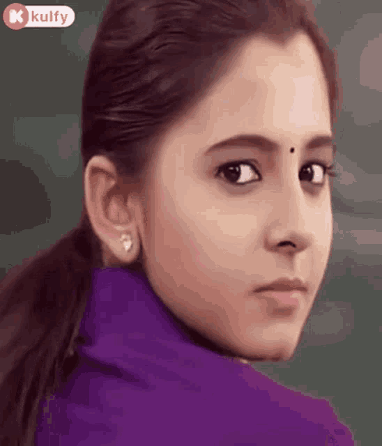 a close up of a woman 's face with a purple shirt and earrings .
