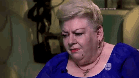 a woman wearing a blue shirt and a necklace is crying .