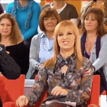 a woman in a floral shirt sits in front of a group of women