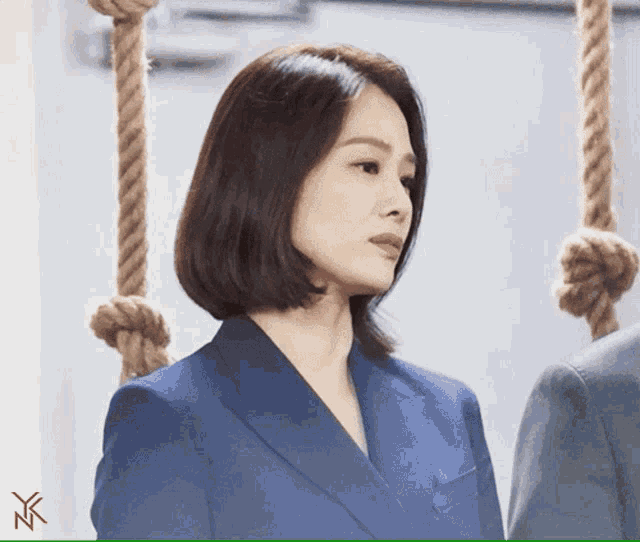 a woman in a blue suit stands in front of ropes hanging from a wall