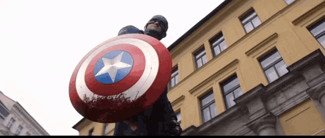 a man in a captain america costume holds a shield in front of a building