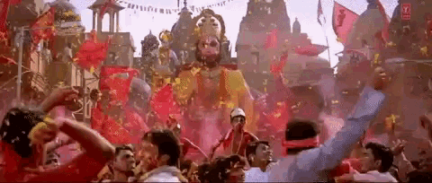 a crowd of people are dancing in front of a large statue of a god .