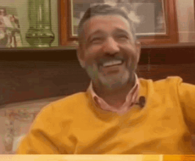 a man with a beard wearing a yellow sweater smiles
