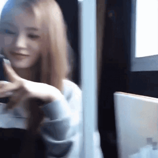a woman with long blonde hair is taking a selfie with her cell phone .