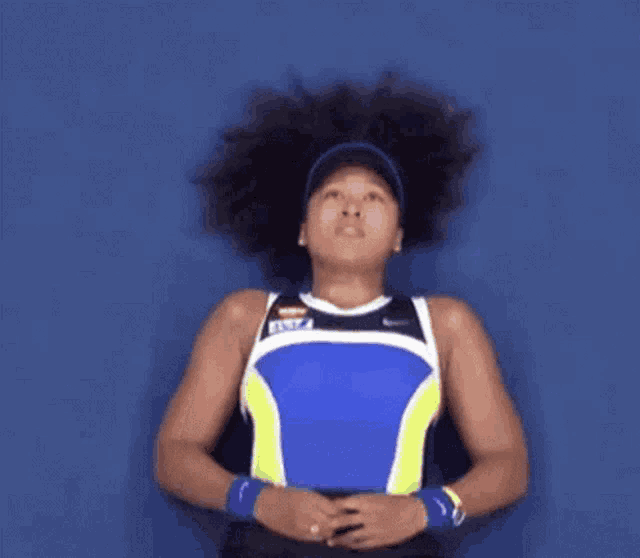 a woman with curly hair is laying on her stomach on a blue surface looking up .