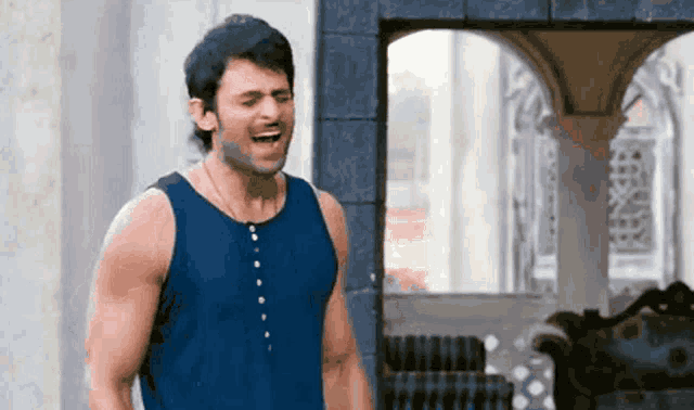 a man in a blue tank top is laughing in front of a window .