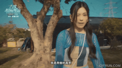 a woman in a blue top stands in front of a tree with gifrun.com written on the bottom