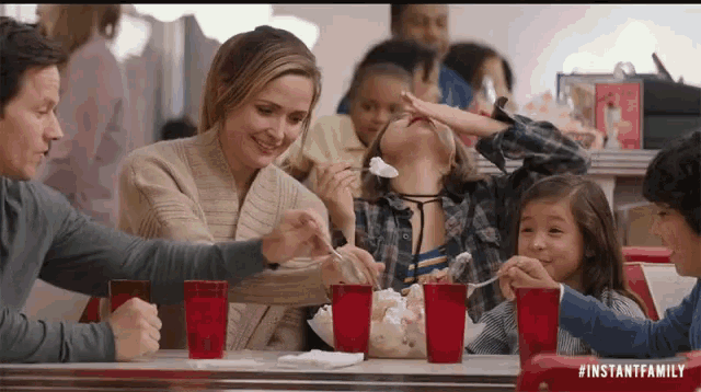 a family is sitting at a table eating ice cream .