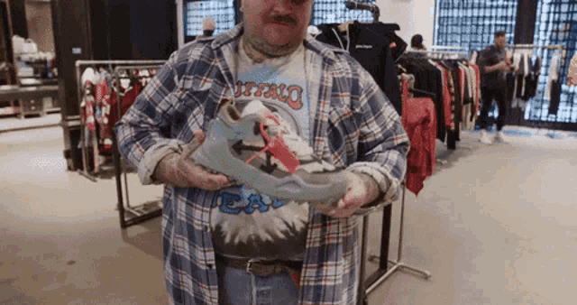 a man in a plaid shirt is holding a pair of shoes in his hands