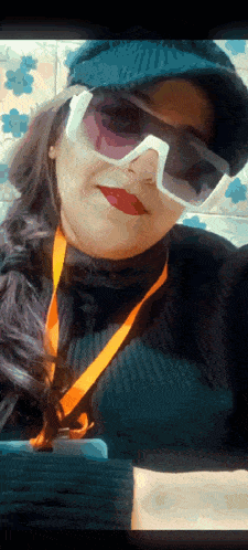 a woman wearing sunglasses and a hat is holding a cell phone .