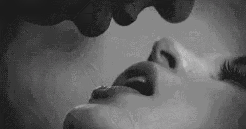 a black and white photo of a man kissing a woman 's lips .