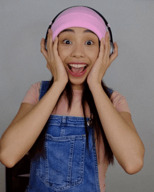 a woman wearing headphones and a pink headband holds her hands to her face