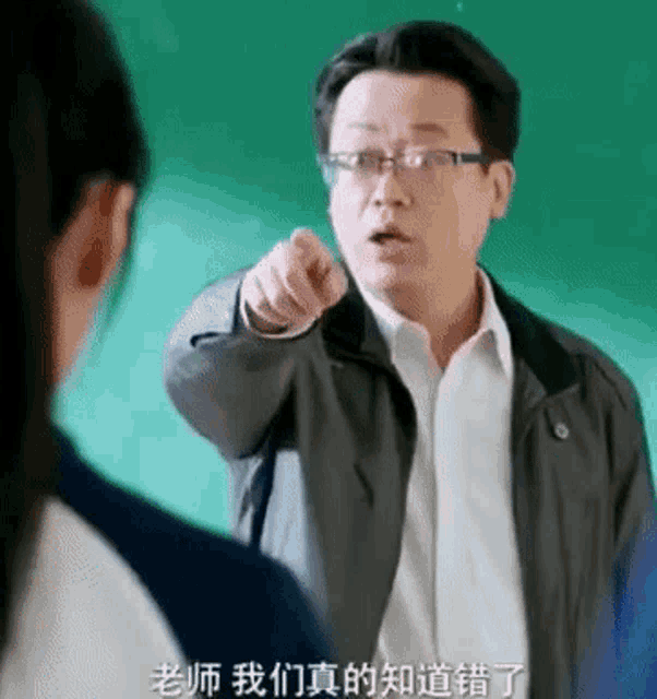 a man in glasses is pointing at a girl in front of a green board