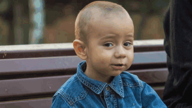 a young boy with a shaved head wearing a denim shirt