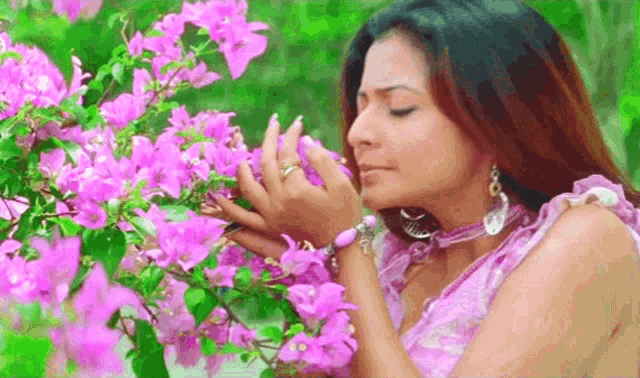 a woman in a pink dress is smelling a bush of pink flowers