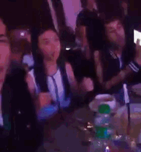 a blurry picture of people sitting at a table with a green bottle of beer in the foreground