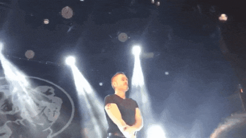 a man in a black shirt stands on a stage in front of a logo for a band