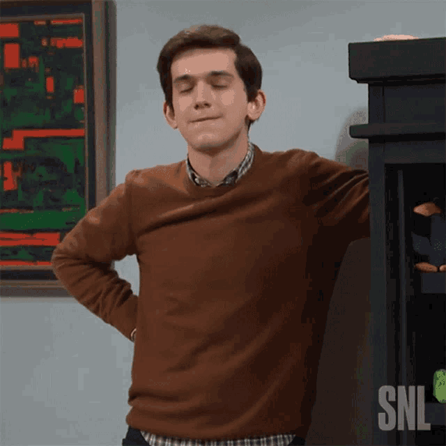 a man wearing a brown sweater is standing in front of a snl sign