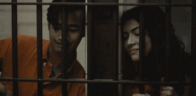 a man in an orange jumpsuit is behind bars in a prison cell