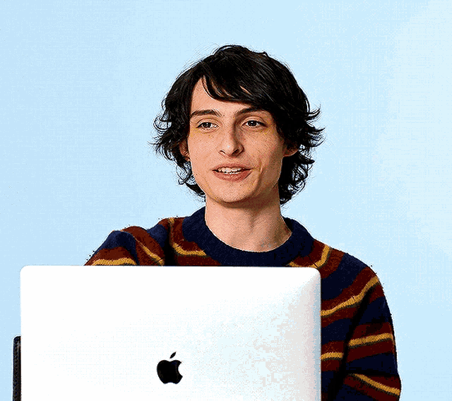a young man wearing a striped sweater is holding an apple laptop