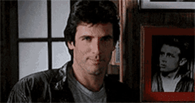 a man in a leather jacket is standing in front of a picture of a man