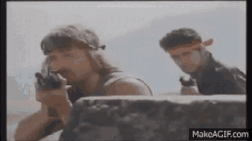 two men are standing next to each other holding guns in a movie scene .