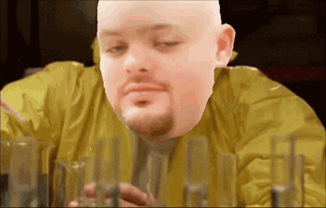 a bald man with a beard is looking at beakers in a lab