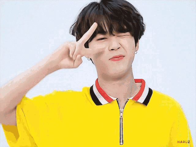 a young man wearing a yellow shirt is making a peace sign with his fingers