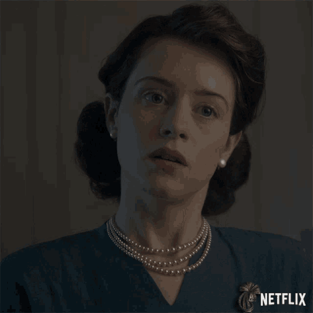 a woman with a pearl necklace and a netflix brooch