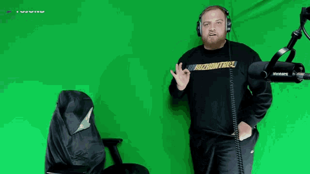a man wearing headphones is standing in front of a green screen with a shure microphone