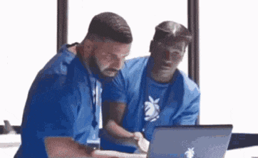 two men in blue shirts are looking at a laptop computer .