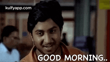 a man is smiling and saying `` good morning '' while standing in front of a window .