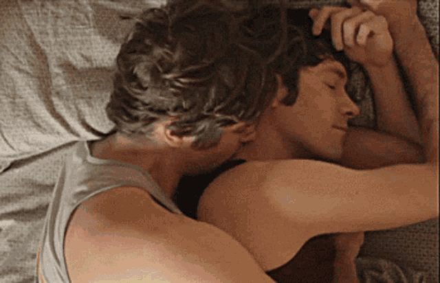 two men are hugging each other on a bed and one is kissing the other on the forehead