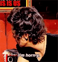 a man sitting in front of a sign that says ' i 'm horn-y ' on it