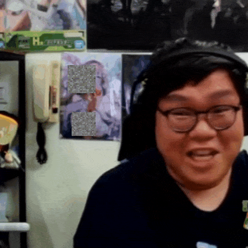 a man wearing headphones and glasses is smiling in front of a wall that has a poster that says ' happiness '