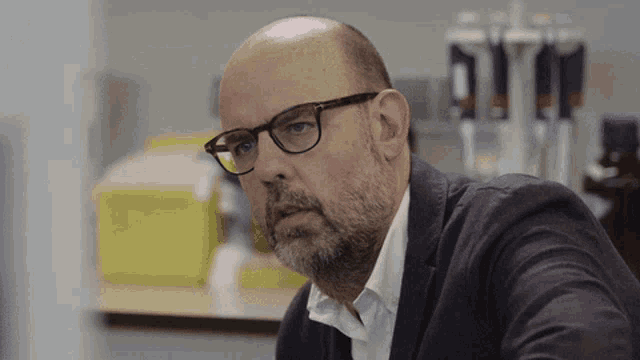 a bald man with glasses and a beard looks to his left