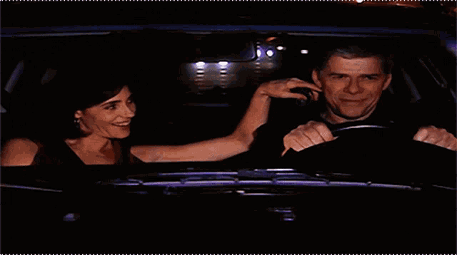 a man and a woman are in a car at night and the woman is touching the man 's ear