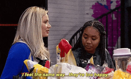 two women are standing next to each other in a room talking .
