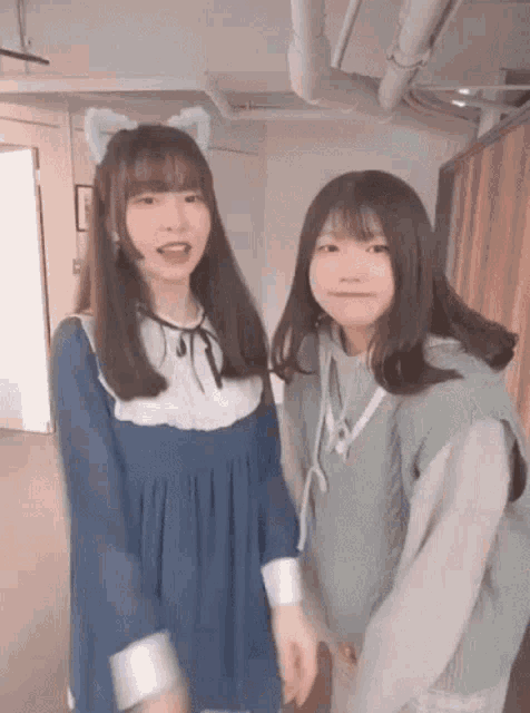 two young girls are standing next to each other in a room . one of the girls is wearing a cat ear headband .