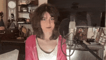 a woman in a pink jacket stands in front of a microphone in front of a television